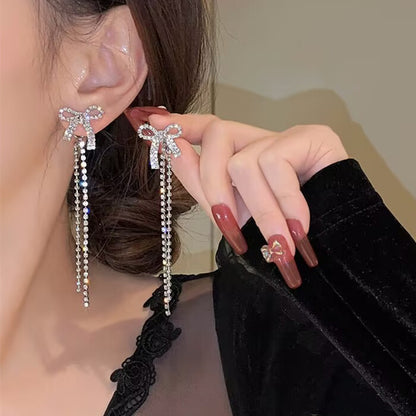 A pair of bow tassel earrings and silver needles.